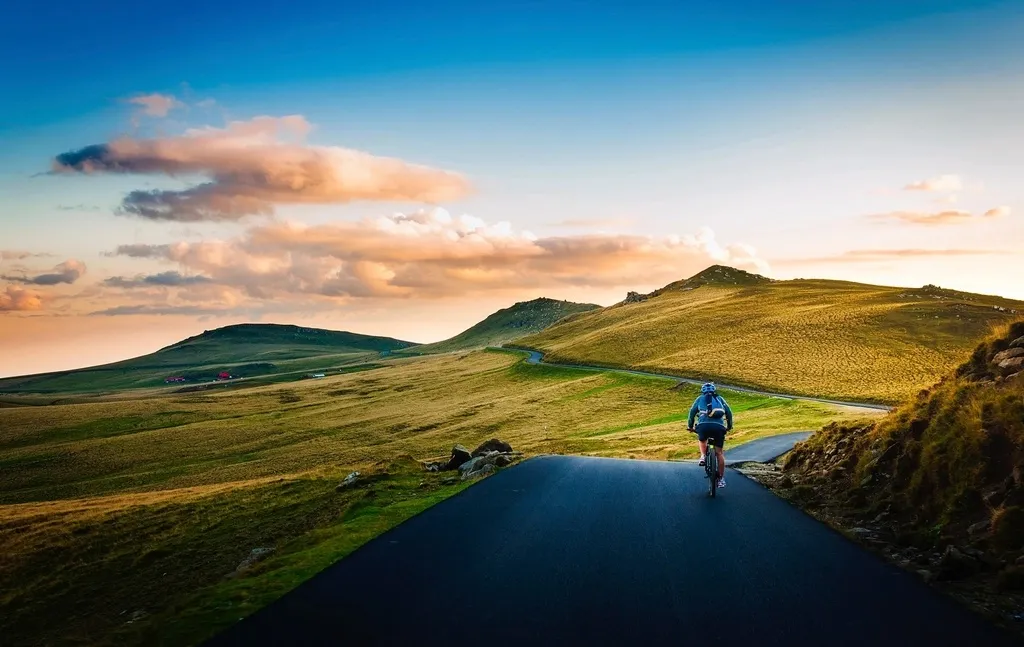 Carretera de montaña desierta al atardecer con una persona pedaleando de espaldas a la cámara