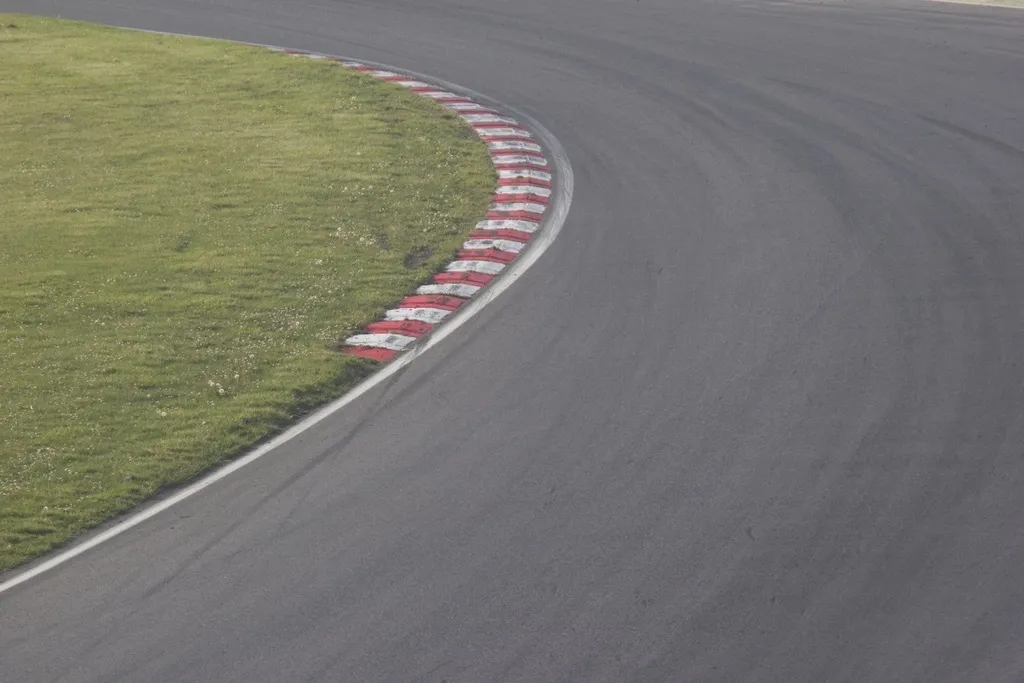 Curva de un circuito de asfalto con pianos rojos y blancos junto a una zona de hierba