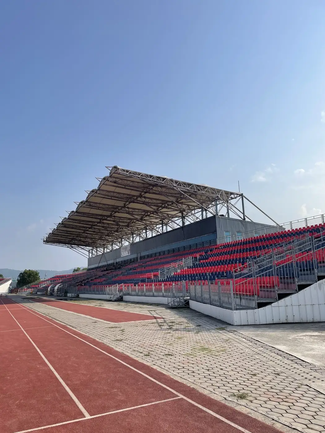 Tribuna cubierta con asientos vacíos junto a una pista de atletismo de color rojo