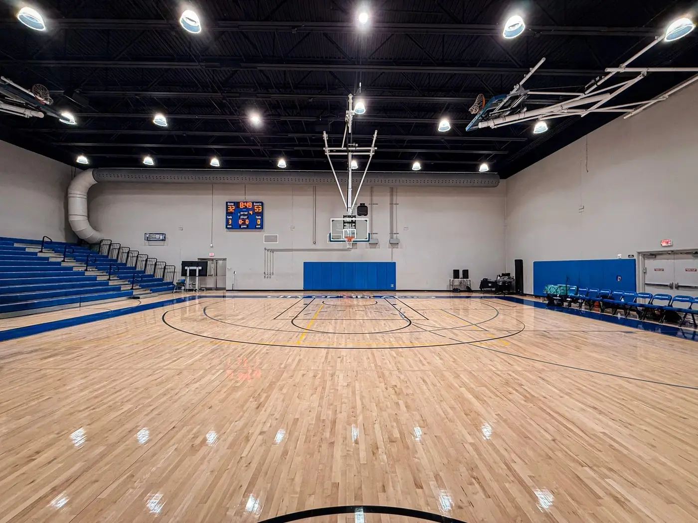 Pista de baloncesto cubierta vacía con parqué brillante, canasta central y gradas plegadas