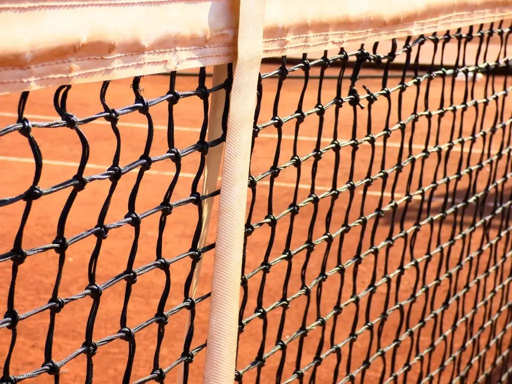 Detalle de una red de tenis tensada sobre una pista de tierra batida iluminada por el sol